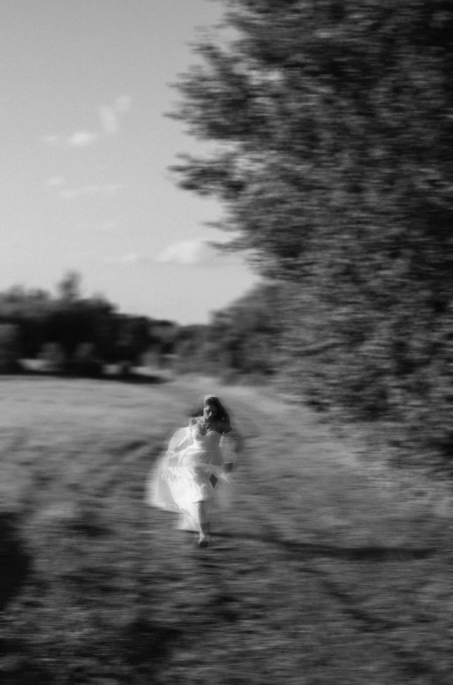 Poruszona czarno-biała fotografia panny młodej biegnącej przez łąkę