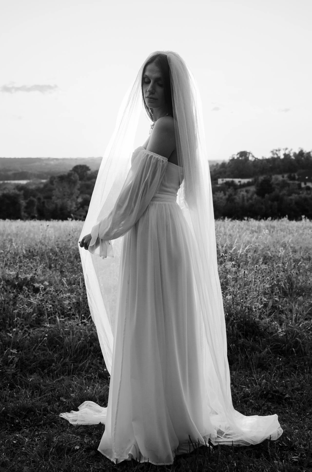 Czarno-biała fotografia panny młodej w długim welonie na tle łąki
