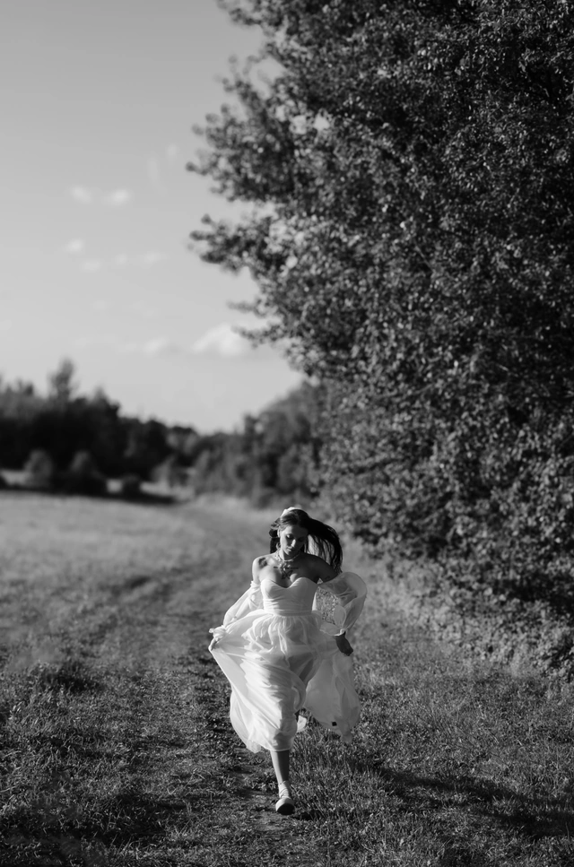 Czarno-biała fotografia panny młodej z rozwianą suknią na łące